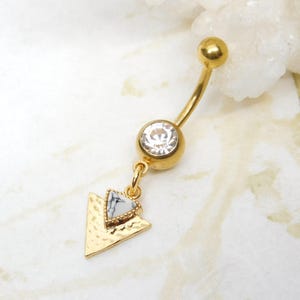 May include: Gold belly button ring with a clear crystal and a dangling triangle charm with a white marble design.