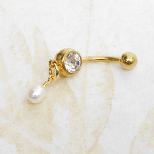 May include: Gold belly button ring with a clear crystal and a dangling pearl charm.