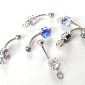 May include: Collection of curved belly button rings with various colored gemstones, including pink, blue, purple, black, and clear. The rings are made of silver-colored metal and have a dangling loop at the bottom.