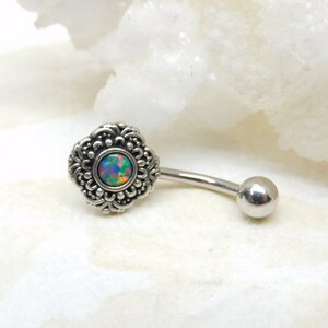 May include: Silver body piercing with a silver ornate flower design and a small iridescent opal gemstone in the center.