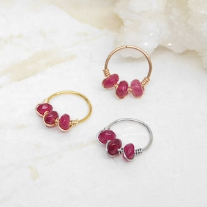May include: Three hoop earrings with three pink gemstone beads each. The hoops are made of gold, rose gold, and silver.