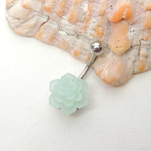 May include: A silver body piercing with a light blue flower charm. The flower charm is made of a sparkly material.