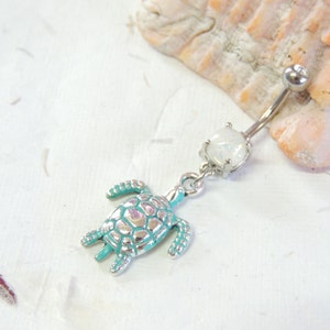 May include: A silver belly button ring with a turquoise and silver turtle charm. The ring features a clear, iridescent stone and a curved barbell design. The turtle charm is detailed with a textured shell.