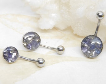 May include: Three silver belly button rings with round, clear, iridescent stones. The stones are filled with small, glittery pieces of blue and silver.