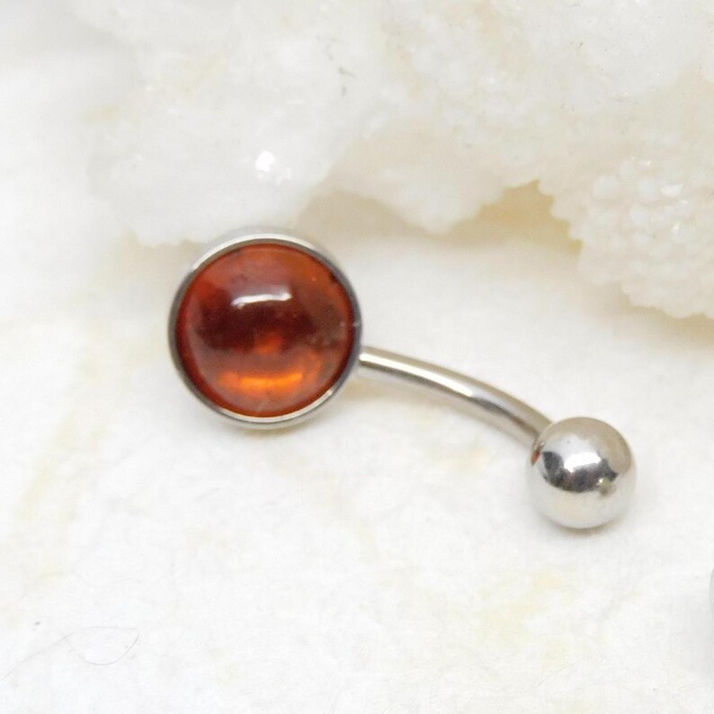 Puede incluir: Un piercing de ombligo plateado con una gema redonda de &aacute;mbar. El anillo es curvo y tiene una peque&ntilde;a bola plateada en el extremo.