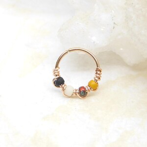 May include: A gold hoop earring with four colorful beads. The beads are black, white, red, and yellow.