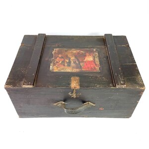 May include: A dark wooden chest with a hinged lid and a metal handle. The chest has a painted scene on the top with figures in red and gold.