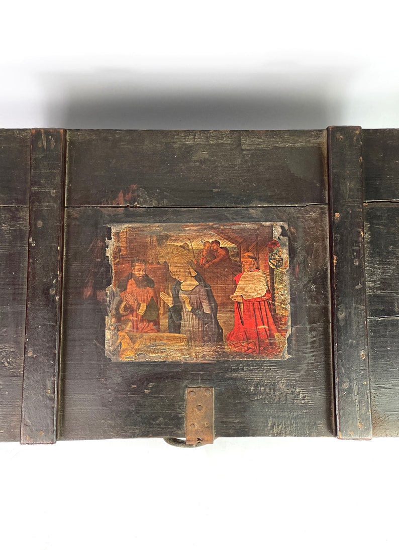 May include: A dark wooden box with a hinged lid. The lid features a painted scene of a religious gathering, with figures in red, blue, and yellow clothing. The box has a metal latch and hinges.