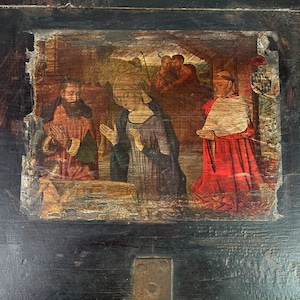 May include: A dark wooden box with a painted scene of the Nativity. The scene depicts Mary, Joseph, and the baby Jesus, with a group of people in the background. The box has a metal latch and hinges.