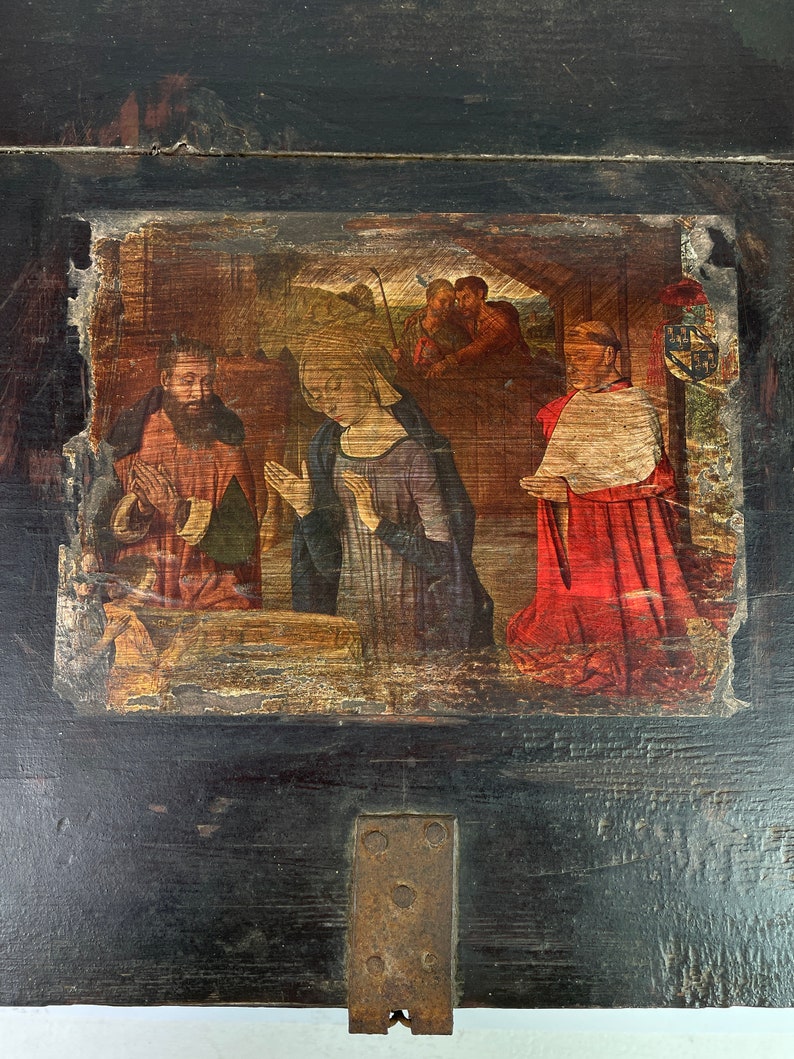 May include: A dark wooden box with a painted scene of the Nativity. The scene depicts Mary, Joseph, and the baby Jesus, with a group of people in the background. The box has a metal latch and hinges.