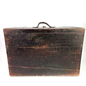 May include: A dark brown wooden box with a metal handle. The box has a worn and weathered appearance, suggesting it is antique.