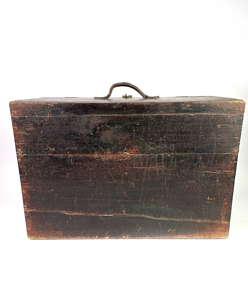 May include: A dark brown wooden box with a metal handle. The box has a worn and weathered appearance, suggesting it is antique.