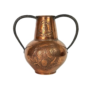 Puede incluir: Un jarrón de cobre con dos asas de hierro negro. El jarrón tiene una textura martillada y está decorado con un diseño en relieve de piñas y hojas.