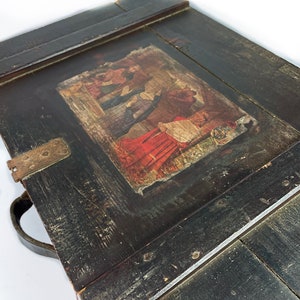 May include: A vintage wooden box with a hinged lid and a leather handle. The lid features a faded, colorful illustration of people in traditional clothing.