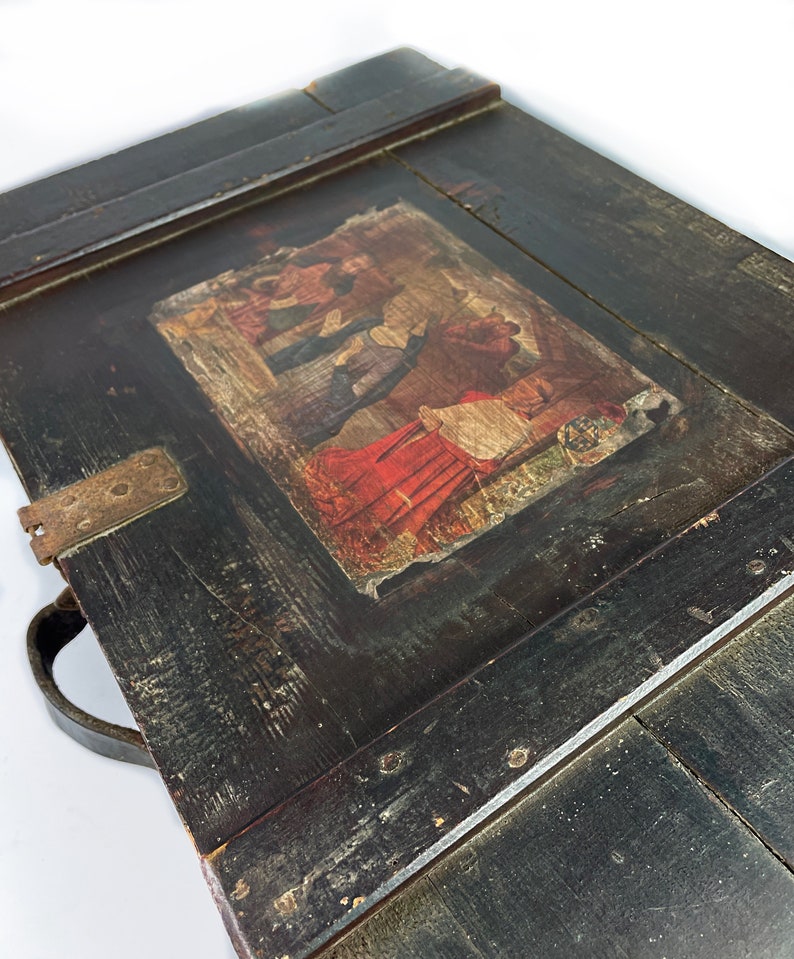 May include: A vintage wooden box with a hinged lid and a leather handle. The lid features a faded, colorful illustration of people in traditional clothing.