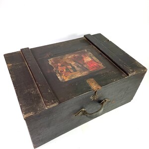 May include: A dark wooden box with a hinged lid and a metal handle. The lid has a painted scene of people in traditional clothing.