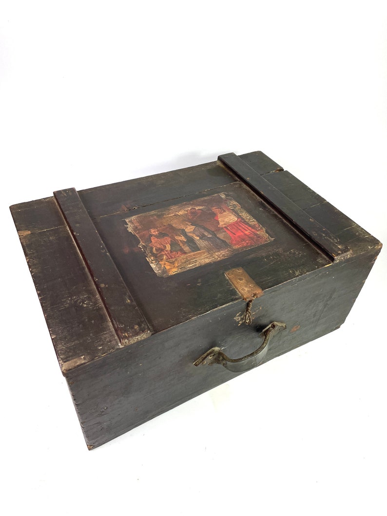 May include: A dark wooden box with a hinged lid and a metal handle. The lid has a painted scene of people in traditional clothing.