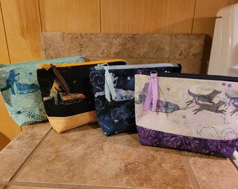 May include: Four zippered pouches with different fabric designs featuring a winter scene with a person or dog pulling a sled. The pouches are lined up in a row on a brown tiled surface.
