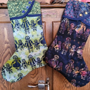 May include: Two Christmas stockings with a blue and white pattern of people holding hands. The stockings are hanging on a wooden door. The stocking on the left has a green and blue fabric cuff. The stocking on the right has a pink and blue fabric cuff.