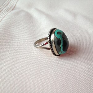 May include: A silver ring with a turquoise and black stone set in a silver bezel.