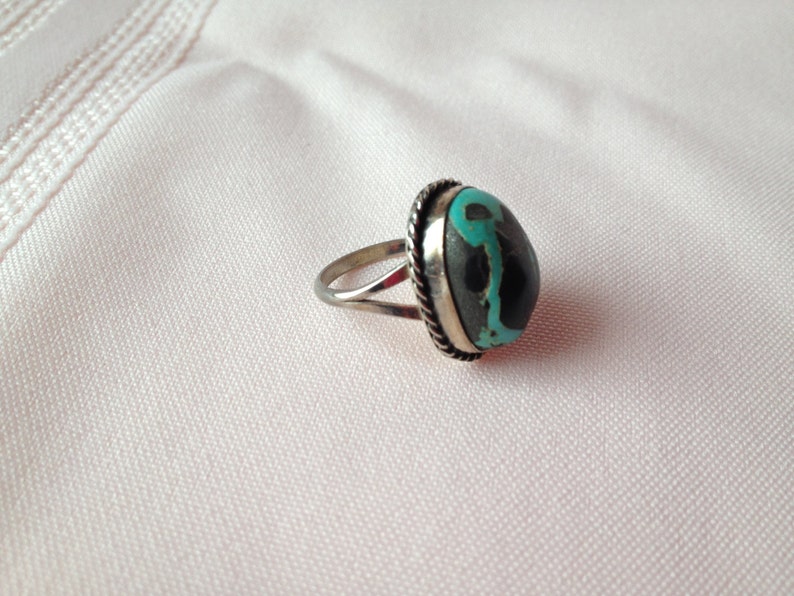 May include: A silver ring with a turquoise and black stone set in a silver bezel.