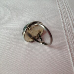 May include: A silver ring with a turquoise stone set in the center. The ring is on a white fabric background.