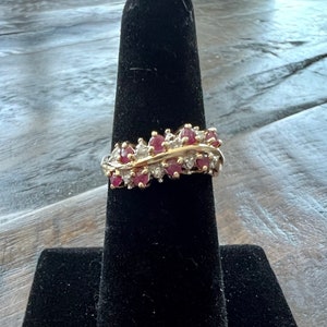 Puede incluir: Un anillo de oro con una fila de piedras preciosas rojas y blancas engastadas en una banda curva.