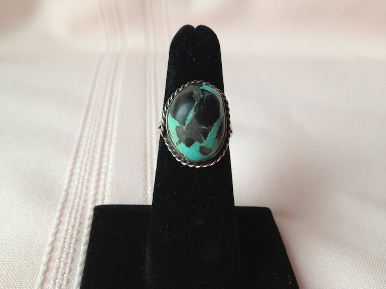 May include: A silver ring with a turquoise and black stone set in a rope-like border.
