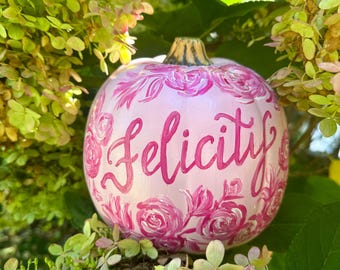 May include: A white pumpkin painted with pink roses and the word "Felicity" in pink script.