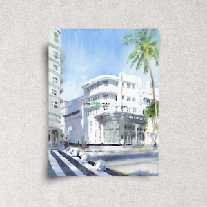 May include: Watercolor painting of a street scene with white buildings, a crosswalk, and a palm tree. The buildings have a distinct art deco style. The sky is a clear blue, and the overall impression is bright and sunny.
