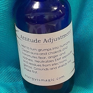 May include: A blue glass bottle with a black spray nozzle and a white label that reads "Attitude Adjustment". The label also includes instructions for use and the website "energyismagic.com".