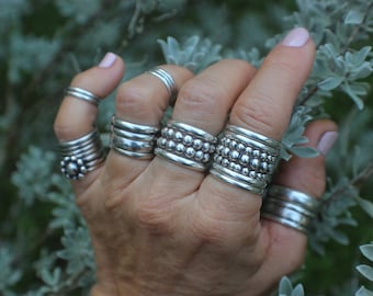 May include: A hand wearing multiple silver rings, some with a beaded design, on each finger.