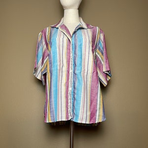 May include: A short-sleeved button-down shirt with a colorful striped pattern in shades of blue, yellow, purple, and pink.