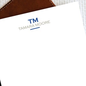 May include: A white sheet of paper with a blue and gray logo. The logo says "TM" in blue and "TAMARA MOORE" in gray.