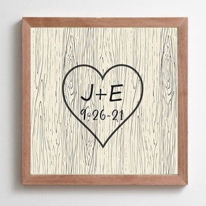Op de afbeelding: Een ingelijst print met een houtnerf achtergrond en een zwart hart met de tekst "J+E 9-26-21" erin.
