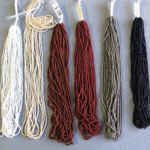 May include: Six strands of seed beads in various colors, including white, cream, red, gray, and black. The beads are strung together in long strands and are ready to be used for jewelry making.