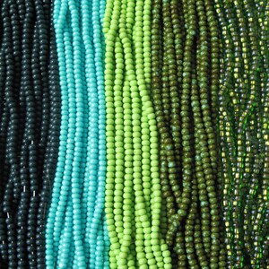 May include: Assortment of green, blue, and black seed beads arranged in rows. The beads are all uniform in size and shape.