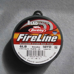 May include: A spool of black FireLine microfused braided bead thread by Berkley. The spool is labeled with the text "6LB Smoke 50YD 0.006in avg. dia FLBT6-42 1389710". The spool is also labeled with the text "The BEADSMITH Carteret, NJ www.beadsmith.com Made in USA".