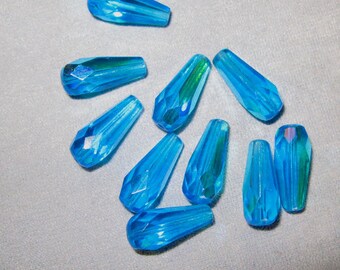 May include: A collection of ten iridescent blue teardrop-shaped glass beads. The beads are faceted and have a shimmery finish.