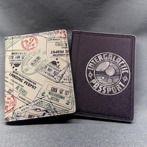 May include: Two passport holders. One is beige with various stamps and the text "Landing Permit". The other is dark blue with the text "Intergalactic Passport" in a circular design.