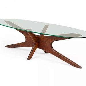 May include: A mid-century modern coffee table with a glass oval top and a unique, starburst-shaped wooden base.