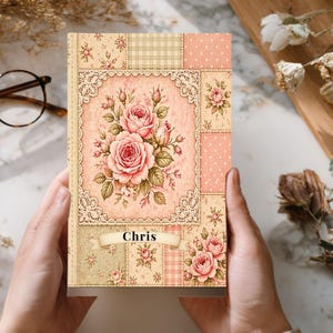 May include: A floral journal with a patchwork design. The cover features a central panel with pink roses, surrounded by lace and set against a light pink background. The name "Chris" is printed on a banner. The journal has a vintage aesthetic.