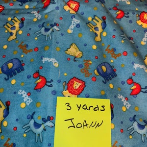 May include: Blue fabric with a repeating pattern of colorful animals, including elephants, lions, birds, and dogs. The fabric is printed with the words "Woof", "Neigh", and "Crack". A yellow sticky note with the text "3 yards JOANN" is attached to the fabric.