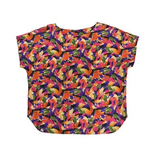 Könnte beinhalten: Eine kurzärmelige, lockere Bluse mit einem farbenfrohen abstrakten Druck in Orange-, Rosa-, Lila-, Grün- und Schwarztönen.