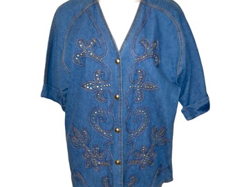 May include: A blue denim shirt with a floral design and gold accents. The shirt has a v-neck and button closure.