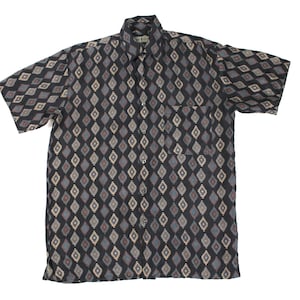 Puede incluir: Camisa de manga corta con un estampado de diamantes en negro, gris y beige. La camisa tiene un bolsillo en el pecho y un cuello clásico. La tela parece ligera, adecuada para climas cálidos.