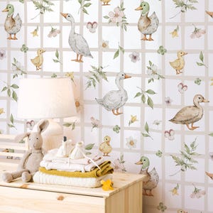 May include: A nursery scene with a light wood dresser, a stuffed bunny, and a stack of folded baby clothes. The wall is decorated with a whimsical wallpaper featuring ducks, geese, flowers, and foliage in a grid pattern. A lamp with a white shade sits on the dresser.