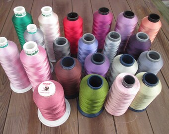 May include: A collection of colorful spools of thread in various shades, including pink, green, red, purple, and gray. The spools are arranged on a wooden surface, showcasing the variety of colors available for sewing and embroidery projects.