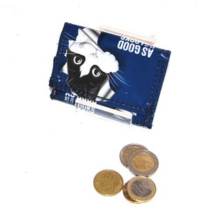 Könnte beinhalten: Eine blaue Brieftasche mit einer schwarz-weißen Katze, die von der Seite herausschaut. Die Brieftasche hat den Text "AS GOOD AS IT LOOKS" aufgedruckt.