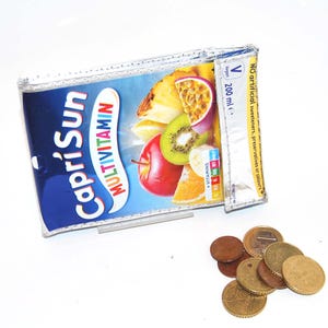 Könnte beinhalten: Eine rechteckige Geldbörse aus einem recycelten Capri Sun Multivitamin-Saftbeutel mit blauem Hintergrund und Abbildungen von Ananas, Passionsfrucht, Kiwi, Apfel und Orange. Der Text lautet Capri Sun Multivitamin und 200 ml. Daneben liegen mehrere verschiedene Metallmünzen.
